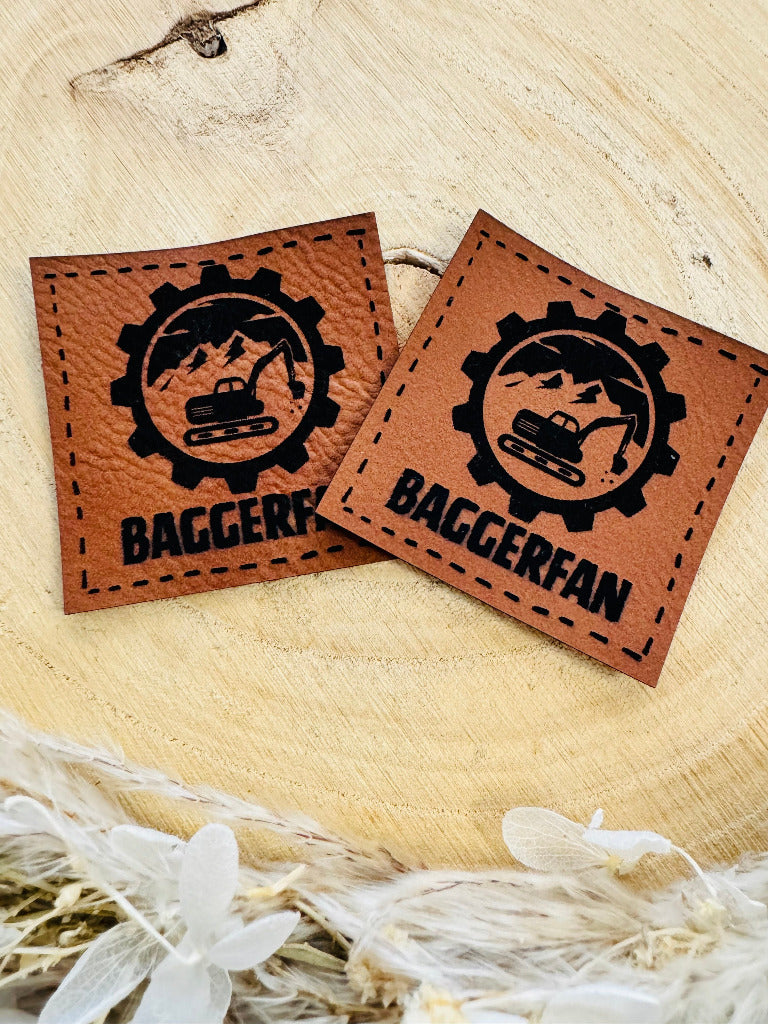 superweiches braunes Kunstlederlabel mit dem Spruch Baggerfan und einem Bagger in einem Zahnrad abgebildet