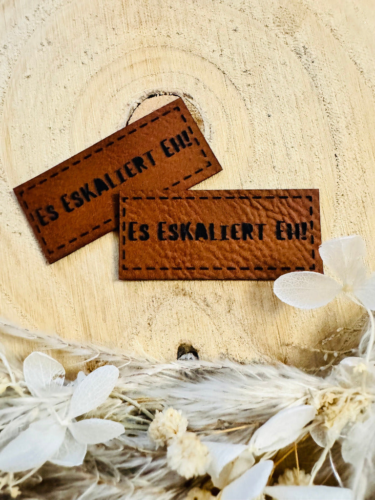 superweiches braunes Kunstlederlabel mit dem Spruch Es eskaliert eh Ausrufezeichen