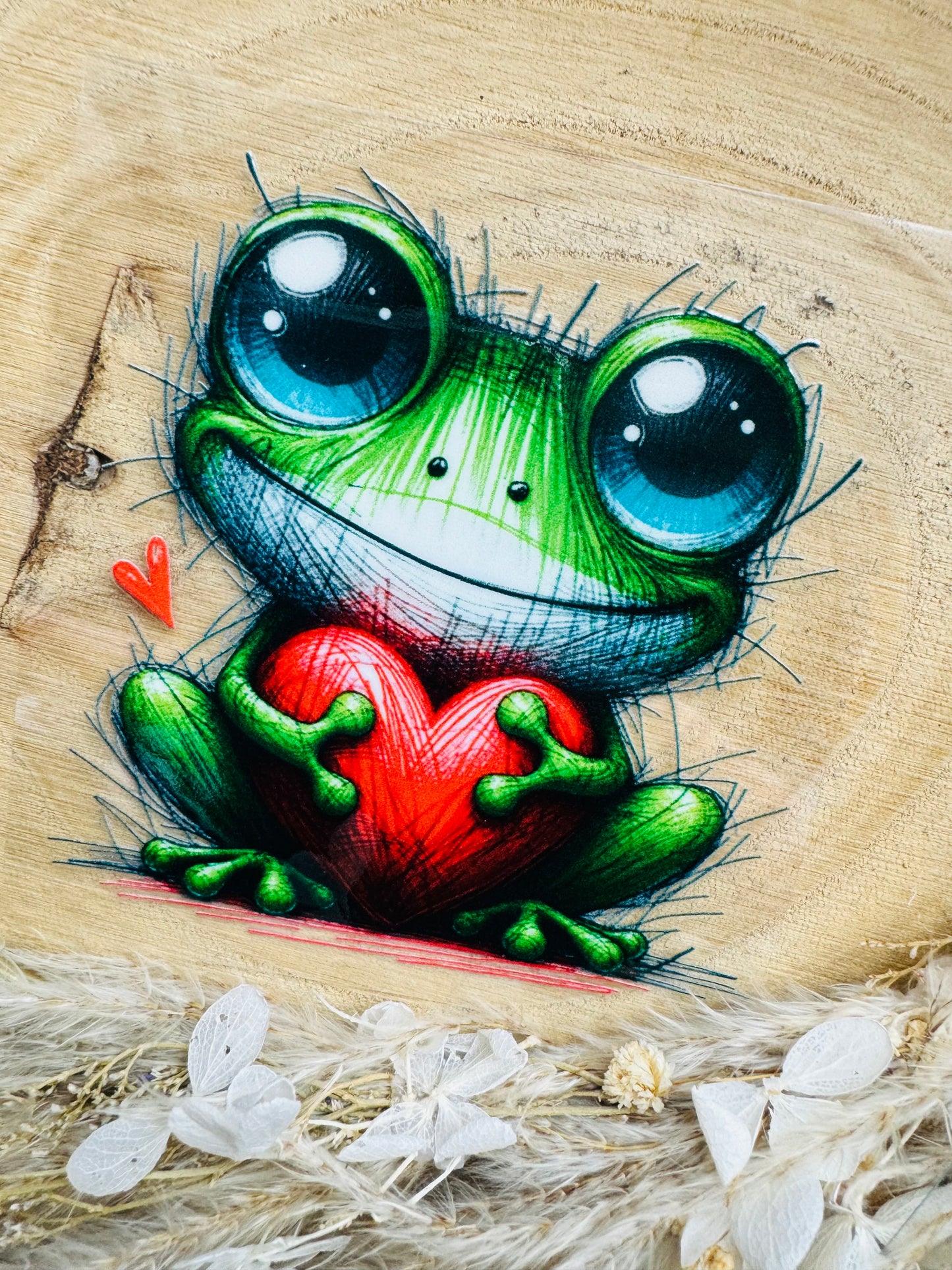 UV-Sticker mit einem kleinen sitzenden Frosch der in seinen Händen ein rotes Herz hält gezeichnet