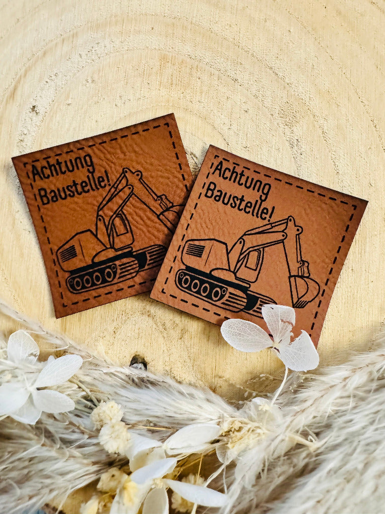 superweiches braunes Kunstlederlabel mit dem Spruch Achtung Baustelle und einem Bagger abgebildet