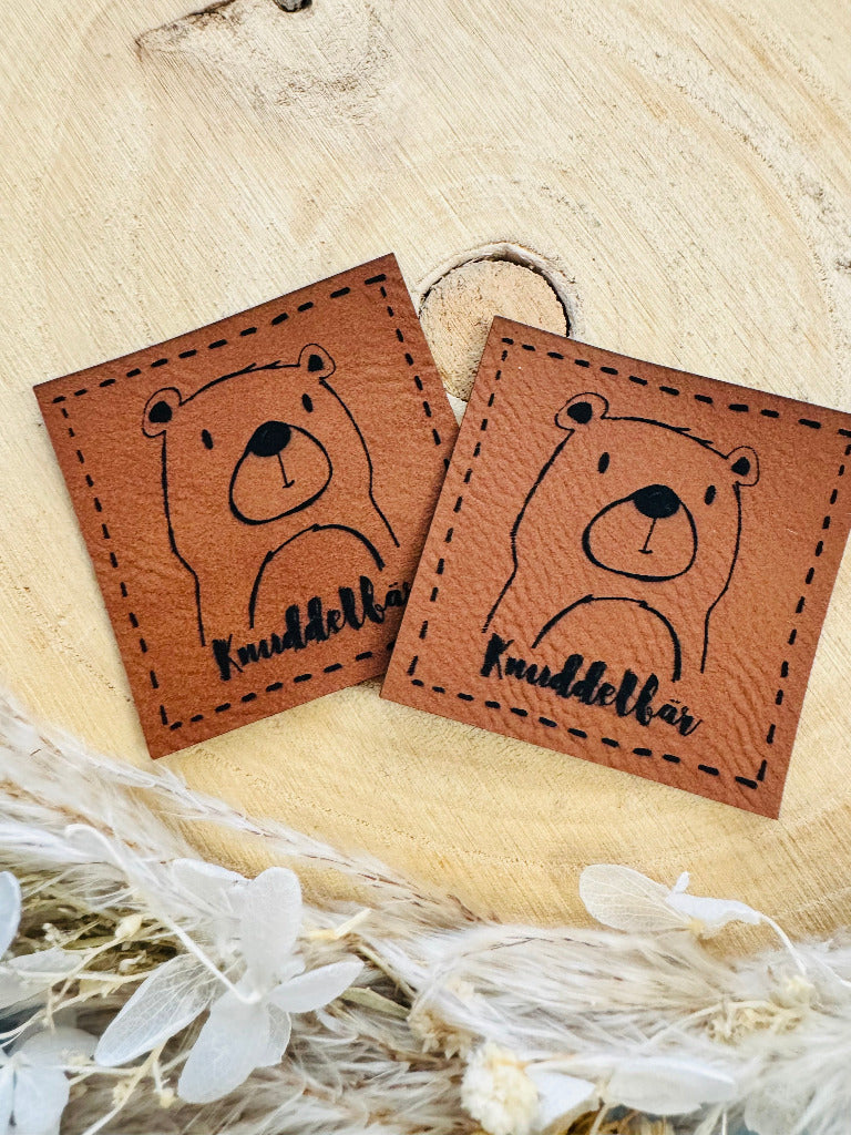 superweiches braunes Kunstlederlabel mit dem Spruch Knuddelbär und einem lustigen Bärengesicht