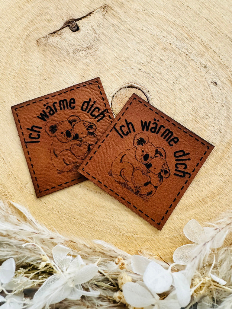 superweiches braunes Kunstlederlabel mit dem Spruch Ich wärme dich und einer abgebildeten Koala Mama mit ihrem Kleinen im Arm