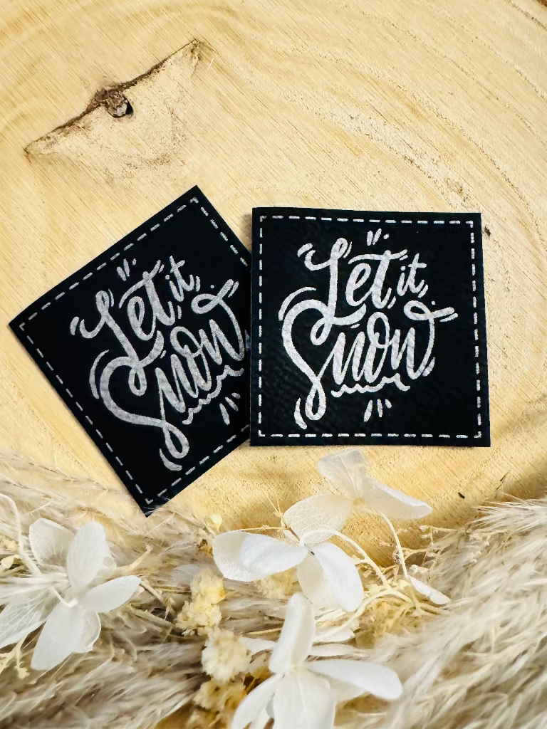 superweiches schwarzes Kunstlederlabel mit dem Spruch Let it Snow in silberner Schrift