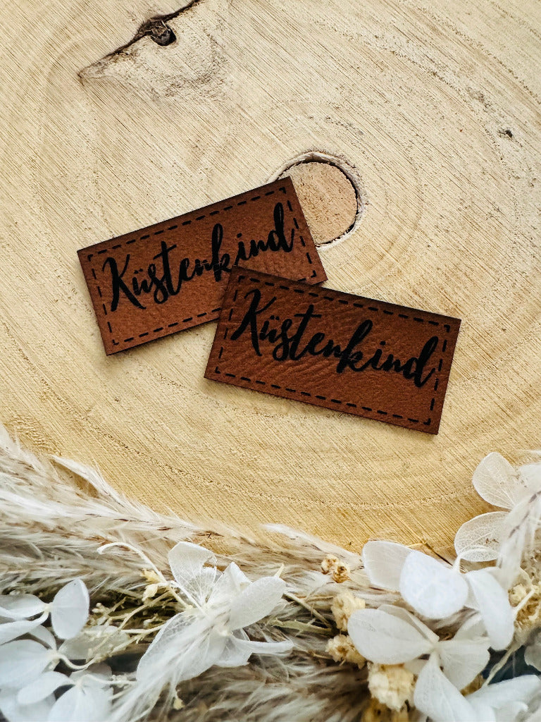 superweiches braunes Kunstlederlabel mit dem Wort Küstenkind in schwarzer Schrift