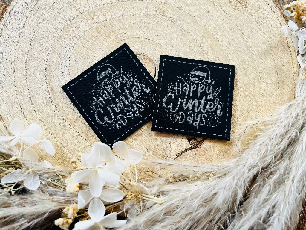 schwarzes Kunstleder Label mit einem kleinen Schneemann und dem Spruch Happy Winter Days in silberner Schrift