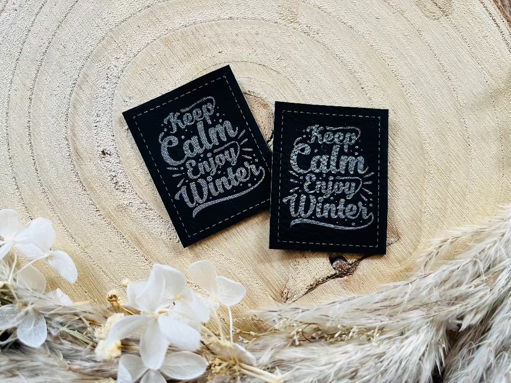 schwarzes Kunstlederlabel mit dem Spruch Keep Calm Enjoy Winter in silberner Schrift