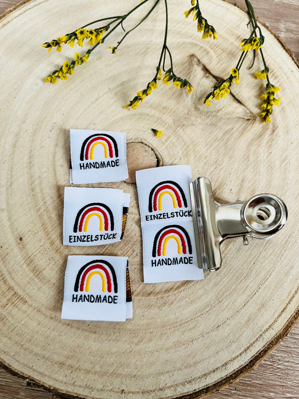 weisses Weblabel mit einem Regenbogen in den Farben schwarz rot gold mit dem Spruch Handmade auf der einen und Einzelstück auf der anderen Seite