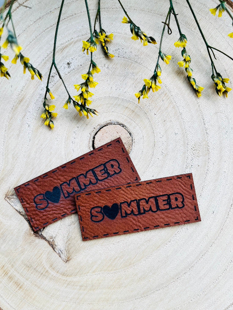 braunes Kunstlederlabel mit dem Wort Sommer, das O ist als Herzchen dargestellt