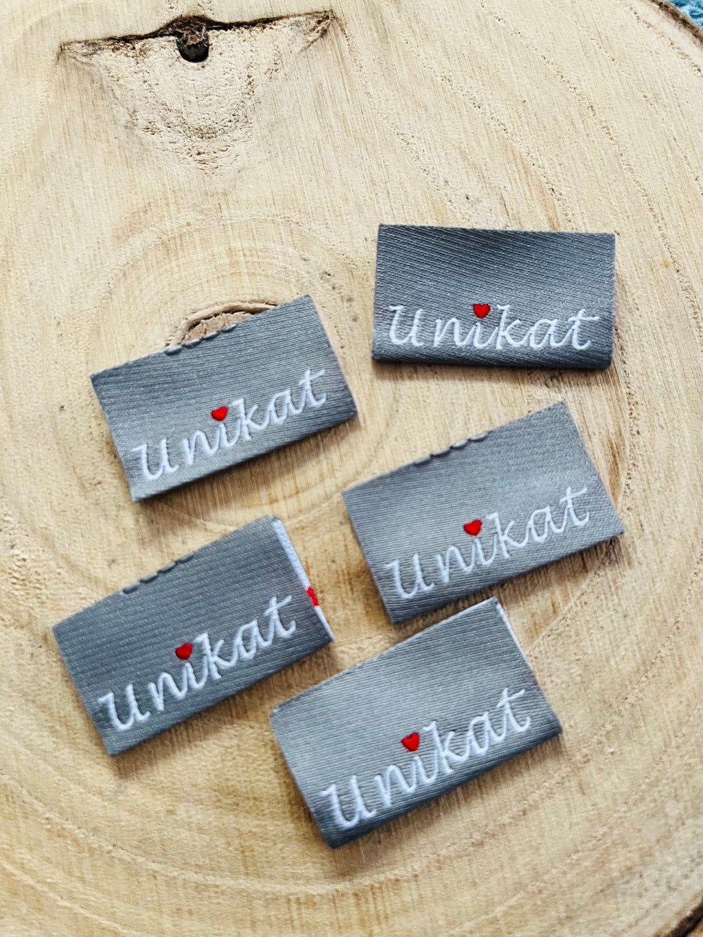 silber graues weblabel mit dem Spruch Unikat in weisser Schrift und einem roten herzchen