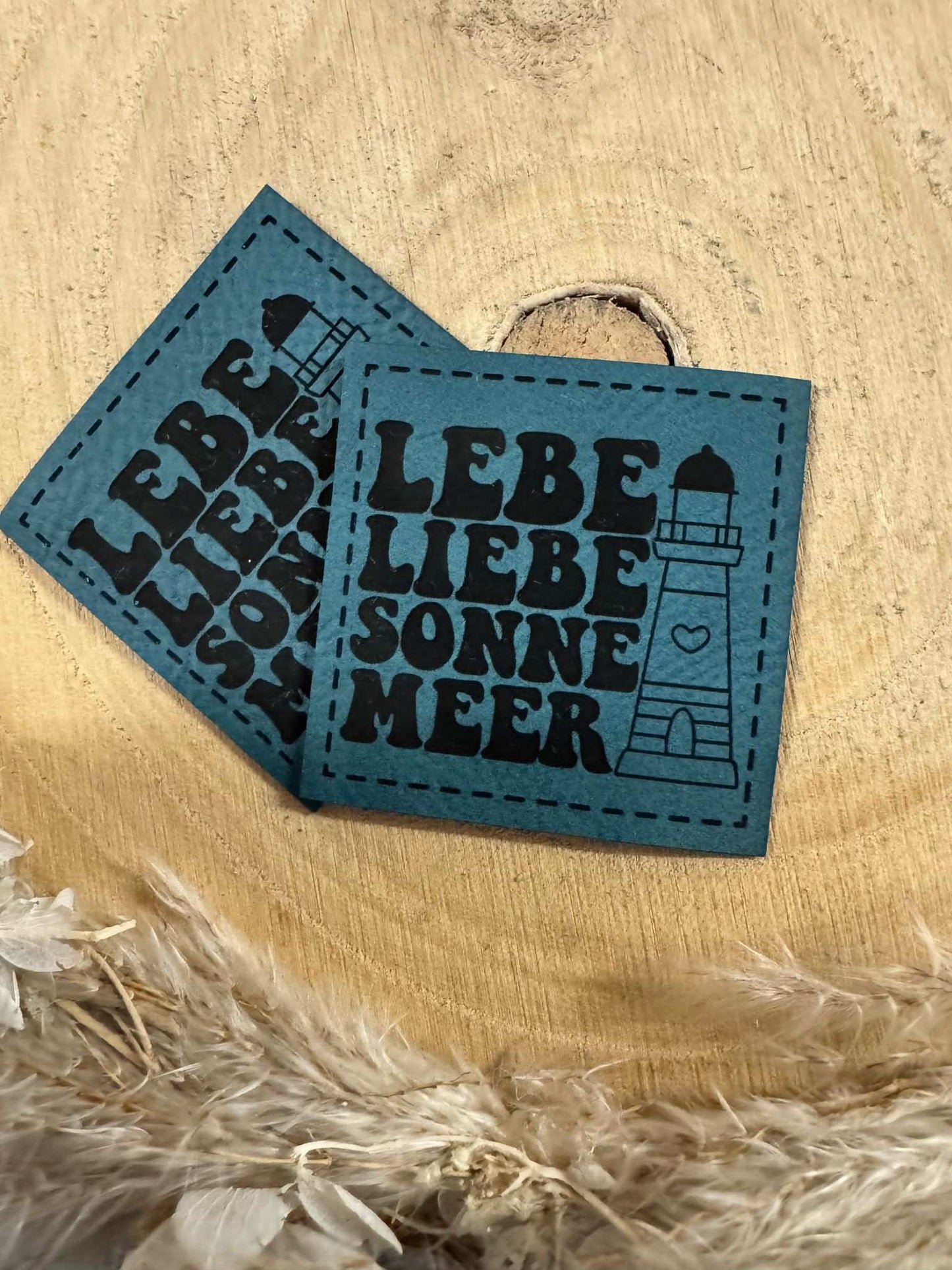 exclusives superweiches türkises Kunstlederlabel mit dem Spruch Lebe Liebe Sonne Meer und einem Leuchtturm abgebildet