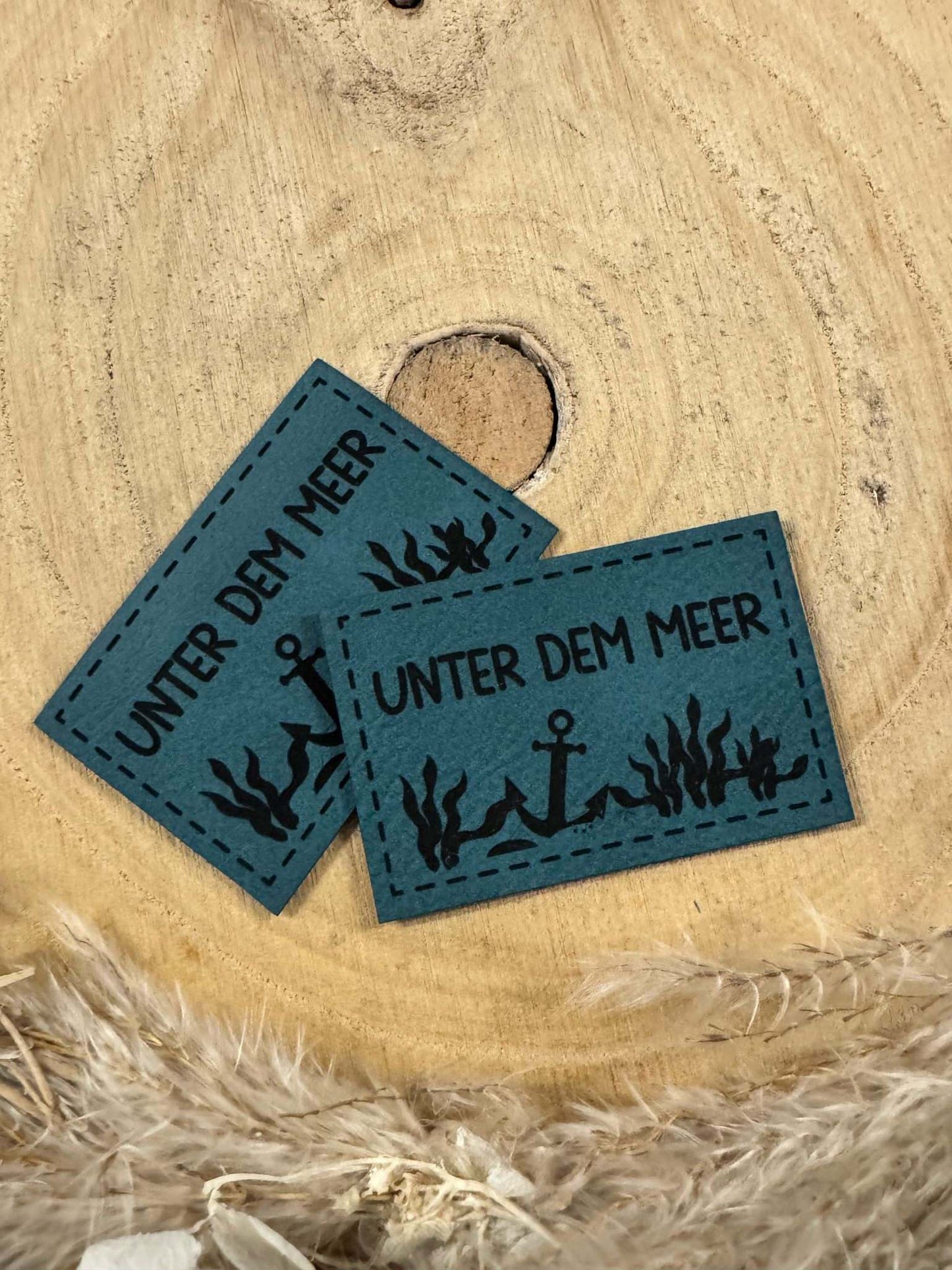 exclusives superweiches Kunstlederlabel in Türkis mit dem Spruch Unter dem Meer und einem Anker auf dem Meeresboden abgebildet