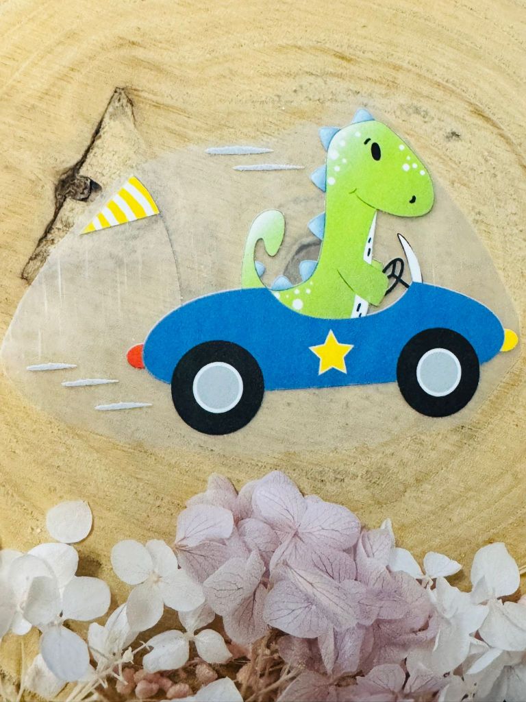 ein tolles Bügelbild aus der Growi Kollektion mit einem Dino in einem blauen Rennauto dargestellt