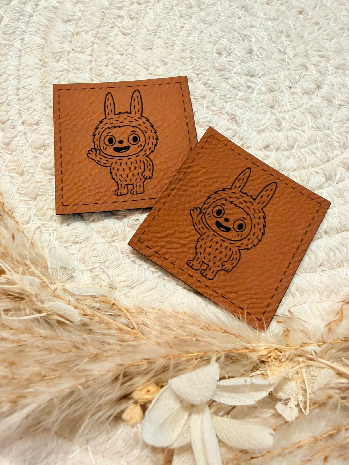 superweiches braunes Kunstlederlabel mit einem kleinen lustigen Monsterchen abgebildet