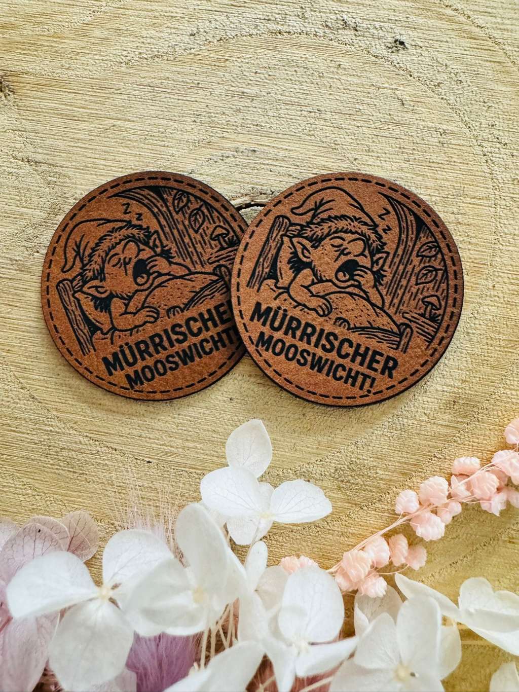 superweiches rundes braunes Kunstlederlabel mit dem Spruch mürrischer Mooswicht und einem kleinen im Bett liegenden Mooswichtel