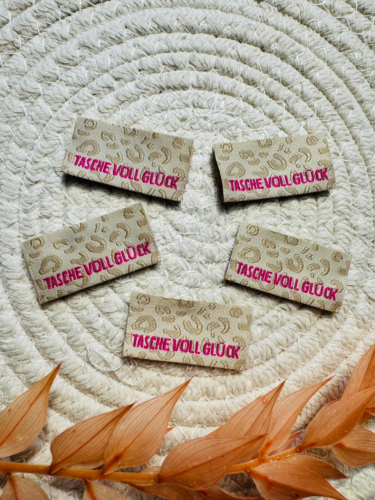 tolles Baumwoll Klapp Weblabel mit dem Spruch Tasche voll Glück auf beigem Leolook Untergrund