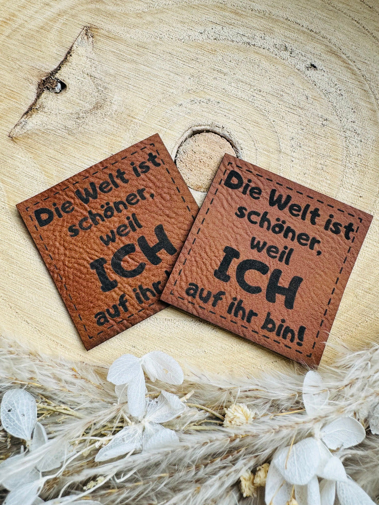 superweiches braunes Kunstlederlabel mit dem Spruch Die Welt ist schöner, weil ich auf ihr bin Ausrufezeichen