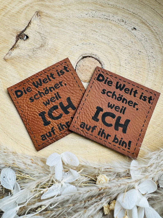 superweiches braunes Kunstlederlabel mit dem Spruch Die Welt ist schöner, weil ich auf ihr bin Ausrufezeichen