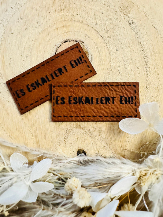 superweiches braunes Kunstlederlabel mit dem Spruch Es eskaliert eh Ausrufezeichen