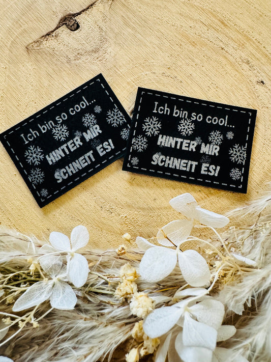 superweiches schwarzes Kunstlederlabel mit dem Spruch Ich bin so cool Punkt punkt Hinter mir schneit es Ausrufezeichen mit kleinen Schneekristallen in silberner Schrift