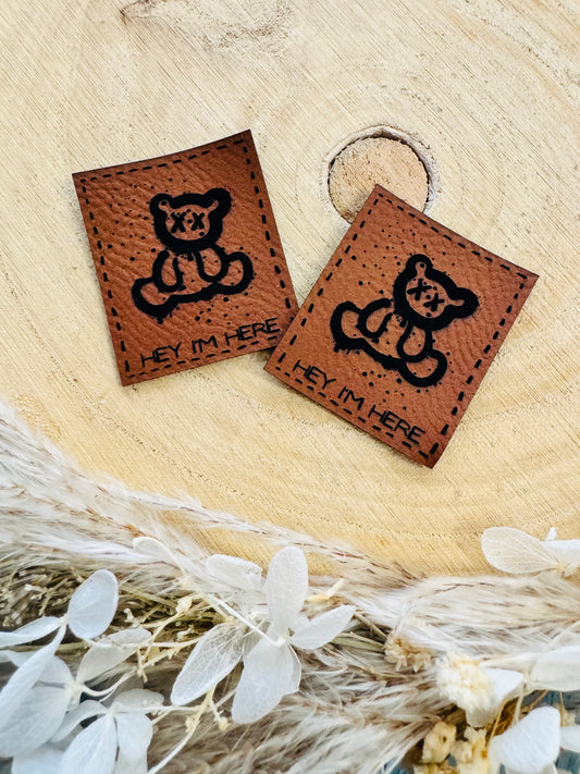 braunes Kunstlederlabel mit dem Spruch Hey im Here und einem kleinen sitzenden Teddy