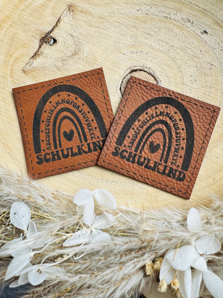 superweiches braunes Kunstlederlabel mit dem Spruch Schulkind unter einem Alphabet Regenbogen