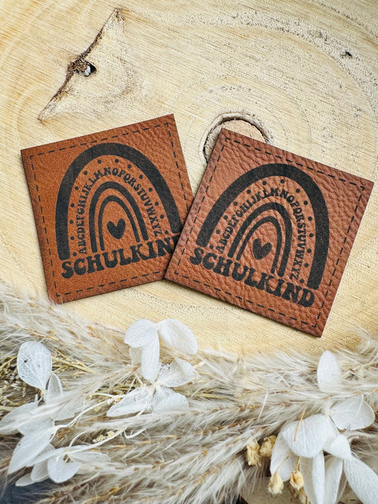 superweiches braunes Kunstlederlabel mit dem Spruch Schulkind unter einem Alphabet Regenbogen