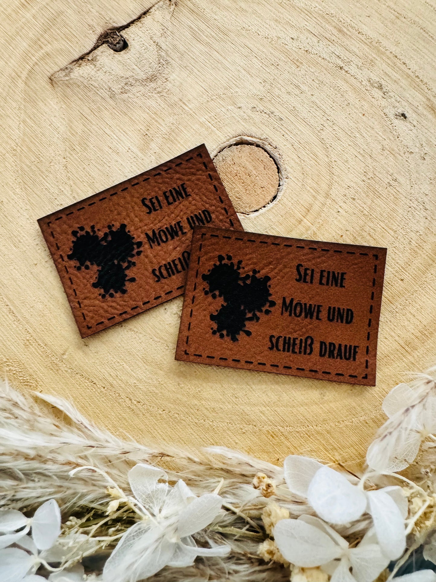 braunes Kunstlederlabel mit dem Spruch Sei eine Möe und scheiß drauf und ...Klecksen