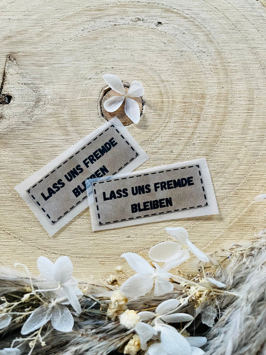 hellgraues Bügellabel mit dem Spruch Lass uns Frmde bleiben