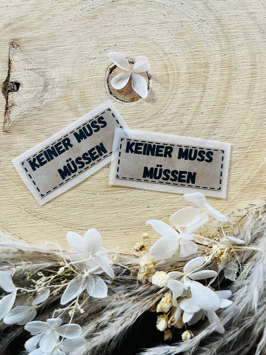 hellgraues Bügellabel mit dem Spruch einer muss müssen in schwarzen Buchstaben