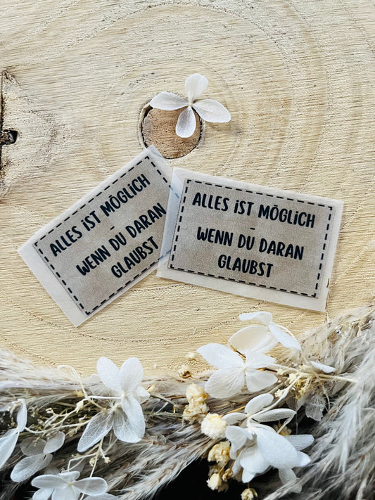 hellgraues Bügellabel mit dem Spruch Alles ist möglich, wenn du daran glaubst  in schwarzer Schrift