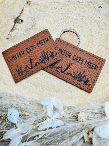 braunes Kunstlederlabel mit dem Spruch Unter dem meer mit einem Anker auf dem Meeresgrund abgebildet