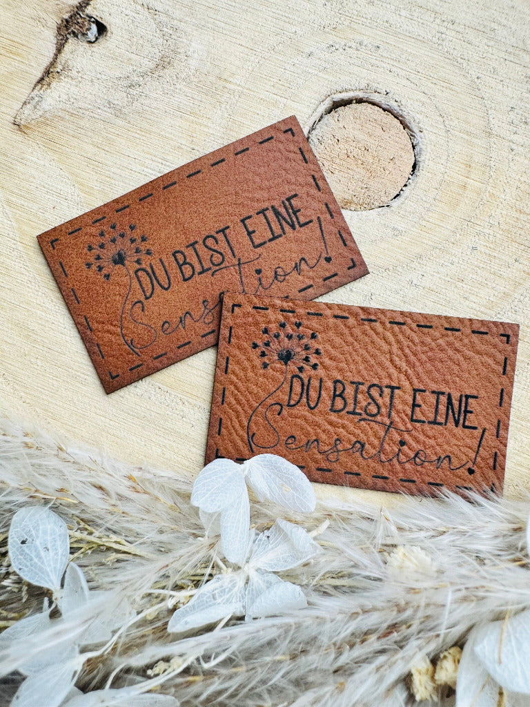 superweiches braunes Kunstlederlabel mit dem Spruch Du bist eine Sensation mit einer abebildeten Pusteblume