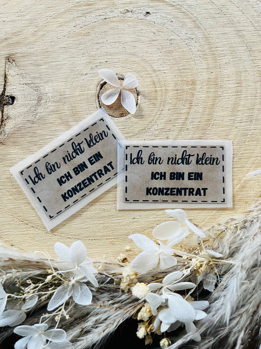 hellgraues Bügellabel mit dem Spruch Ich bin nicht klein, ich bin ein Konzentrat in schwarzer Schrift