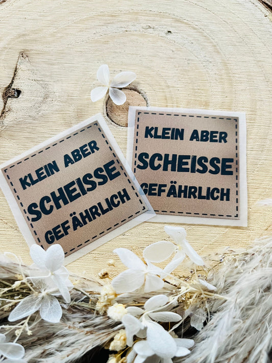 hellbraunes Bügellabel mit dem Spruch Klein aber Scheisse gefährlich