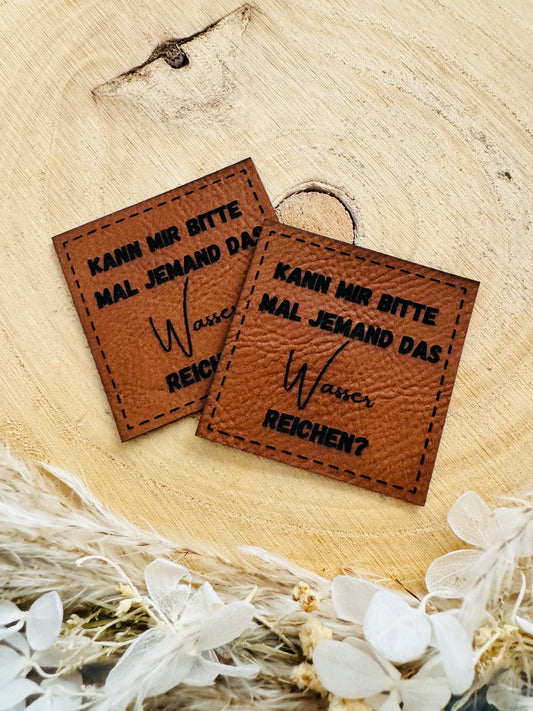 braunes Kunstlederlabel mit dem Spruch Kann mir bitte mal Jemand das Wasser reichen fragezeichen