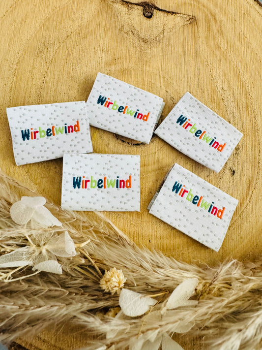 Weblabel graue Punkte auf weissem Untergrund und dem Spruch Wirbelwind in bunten Farben