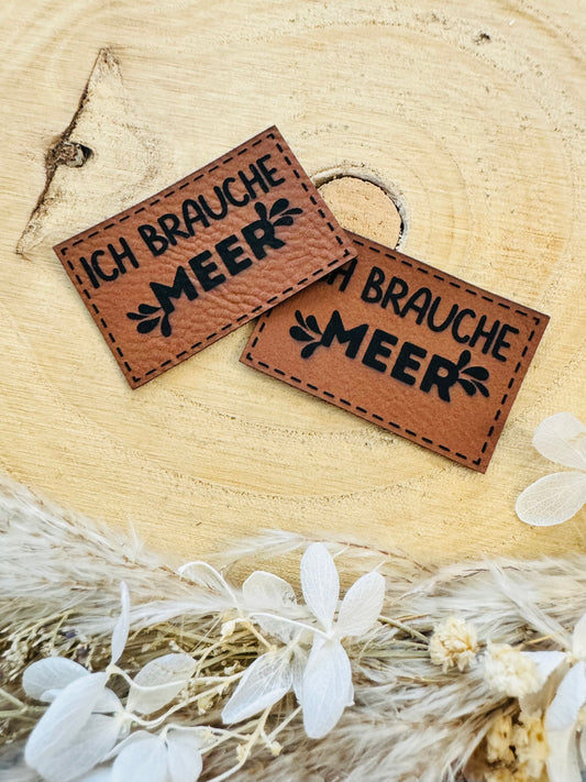 braunes Kunstlederlabel mit dem Spruch ich brauche meer in schwarzer Schrift