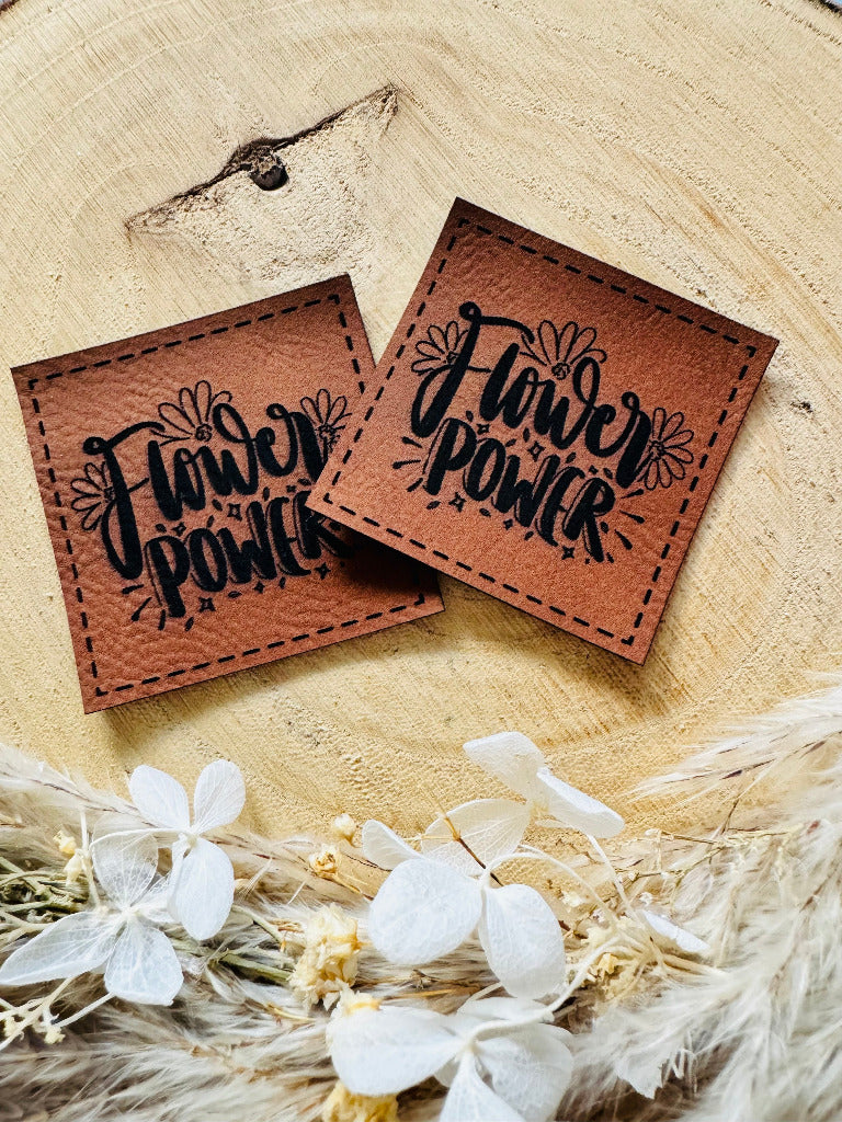 superweiches braunes Kunstlederlabel mit dem Spruch Flower Power umrahmt von Blüten