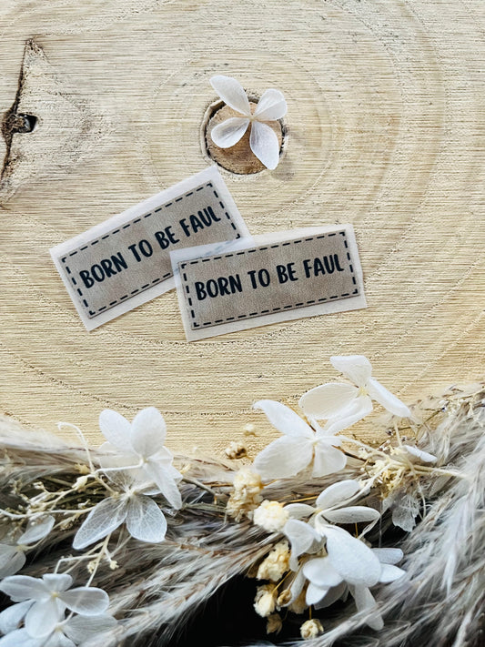 hellgraues Bügellabel mit dem Spruch Born to be Faul in schwarzer schrift