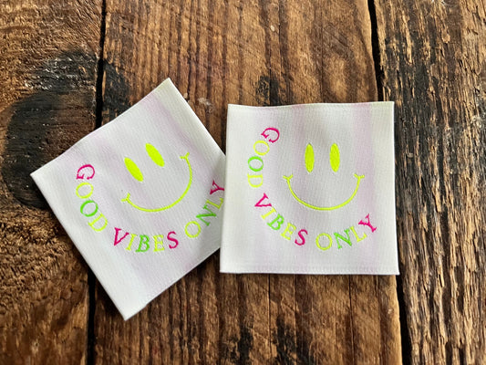 weisses fluoreszierendes XXL Weblabel mit einem lächelnden Smiley und dem Spruch Good Vibes Only in bunten Buchstaben