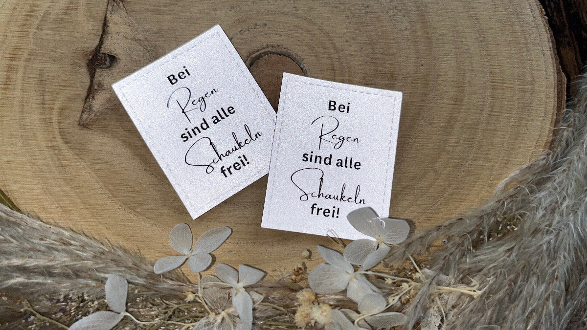 silbernes reflektierendes Kunstlederlabel mit dem Spruch Bei Regen sind alle Schaukeln frei Ausrufezeichen