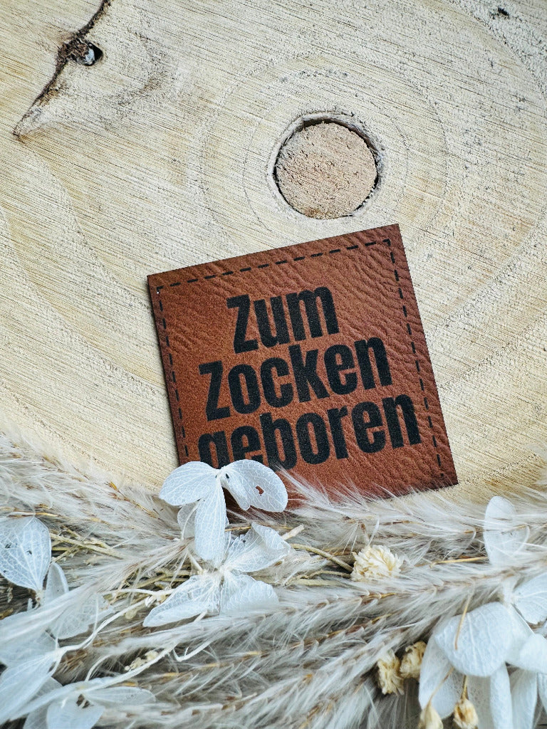 braunes Kunstlederlabel mit dem Spruch Zum Zocken geboren in schwarzen Buchstaben