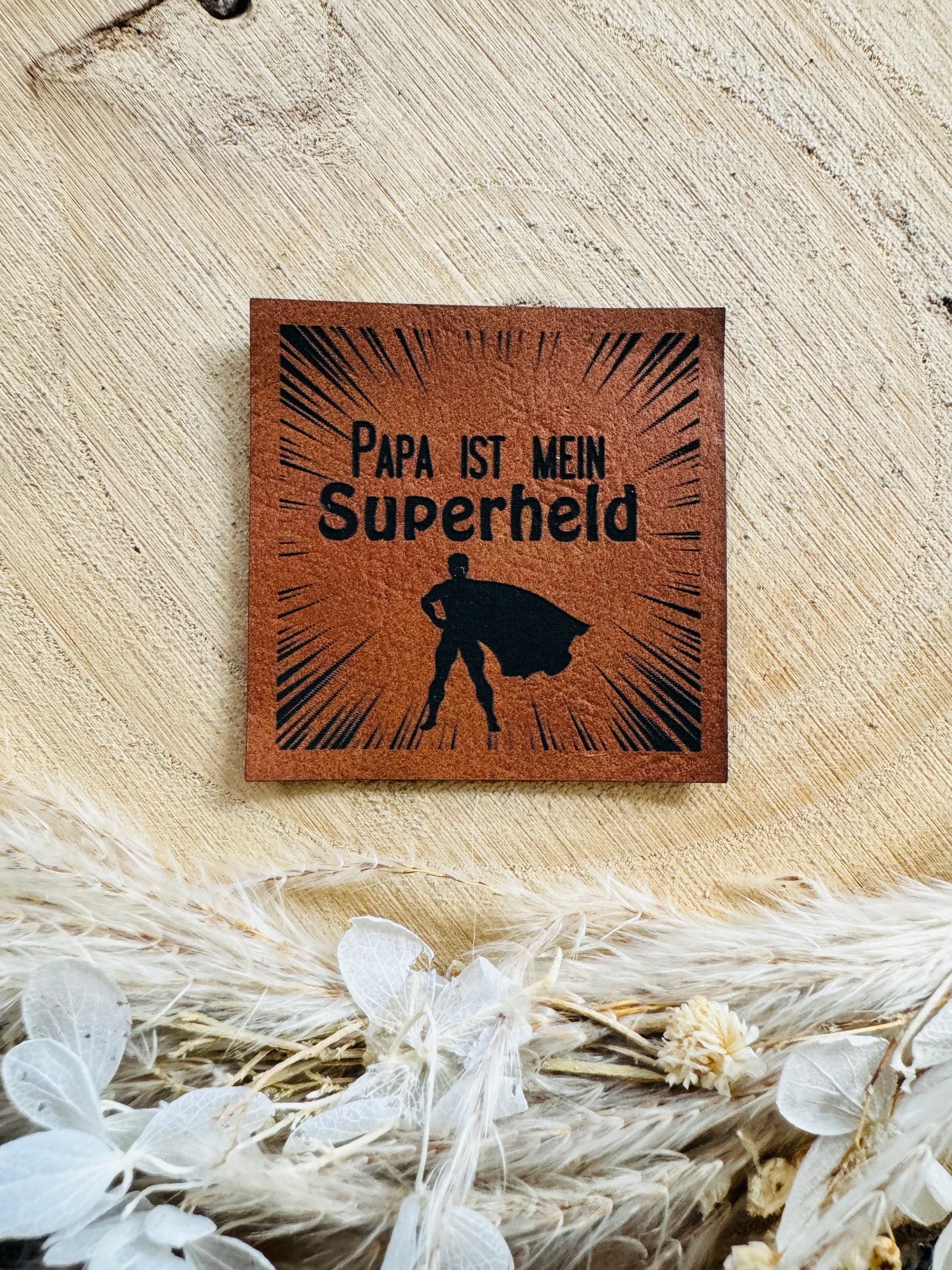 braunes Kunstlederlabel mit einem kleinen Superhlden und dem Spruch Papa ist mein Superheld in schwarzer Schrift