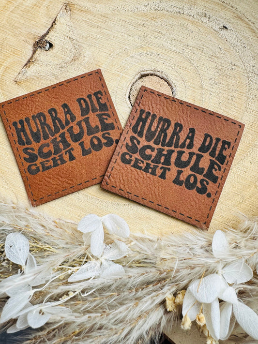 superweiches braunes Kunstlederlabel mit dem Spruch Hurra die Schule geht los in geschwungener schwarzer Schrift