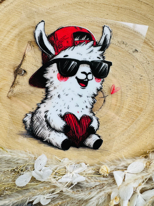 UV-Sticker mit einem kleinen weissen sitzenden Lama mit cooler Sonnenbrille und roten Käppi welches ein rotes Herzchen in seinen Händen hält