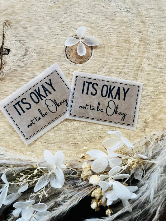 hellgraues Bügellabel mit dem Spruch Its okay not to be Okay in schwarzer Schrift