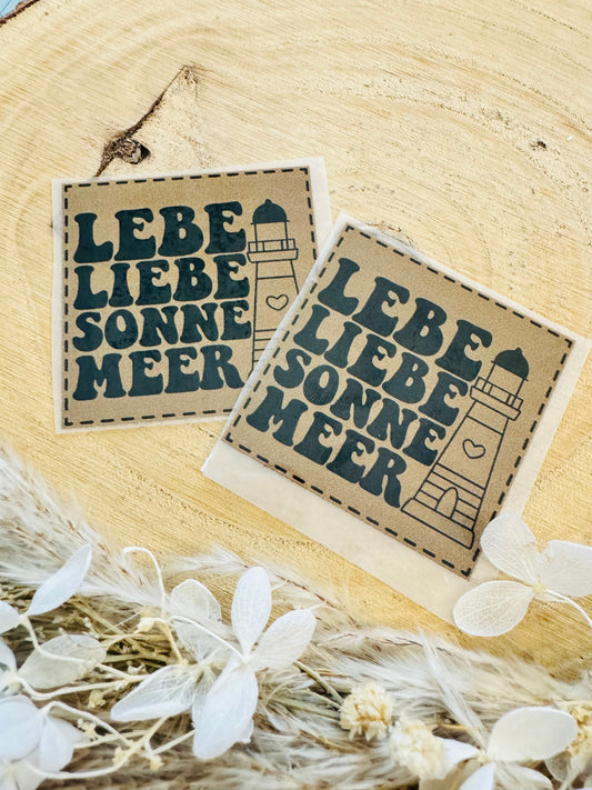 braunes Bügellabel Etikett mit dem Spruch Lebe Liebe Sonne Meer und einem Leuchtturm abgebildet