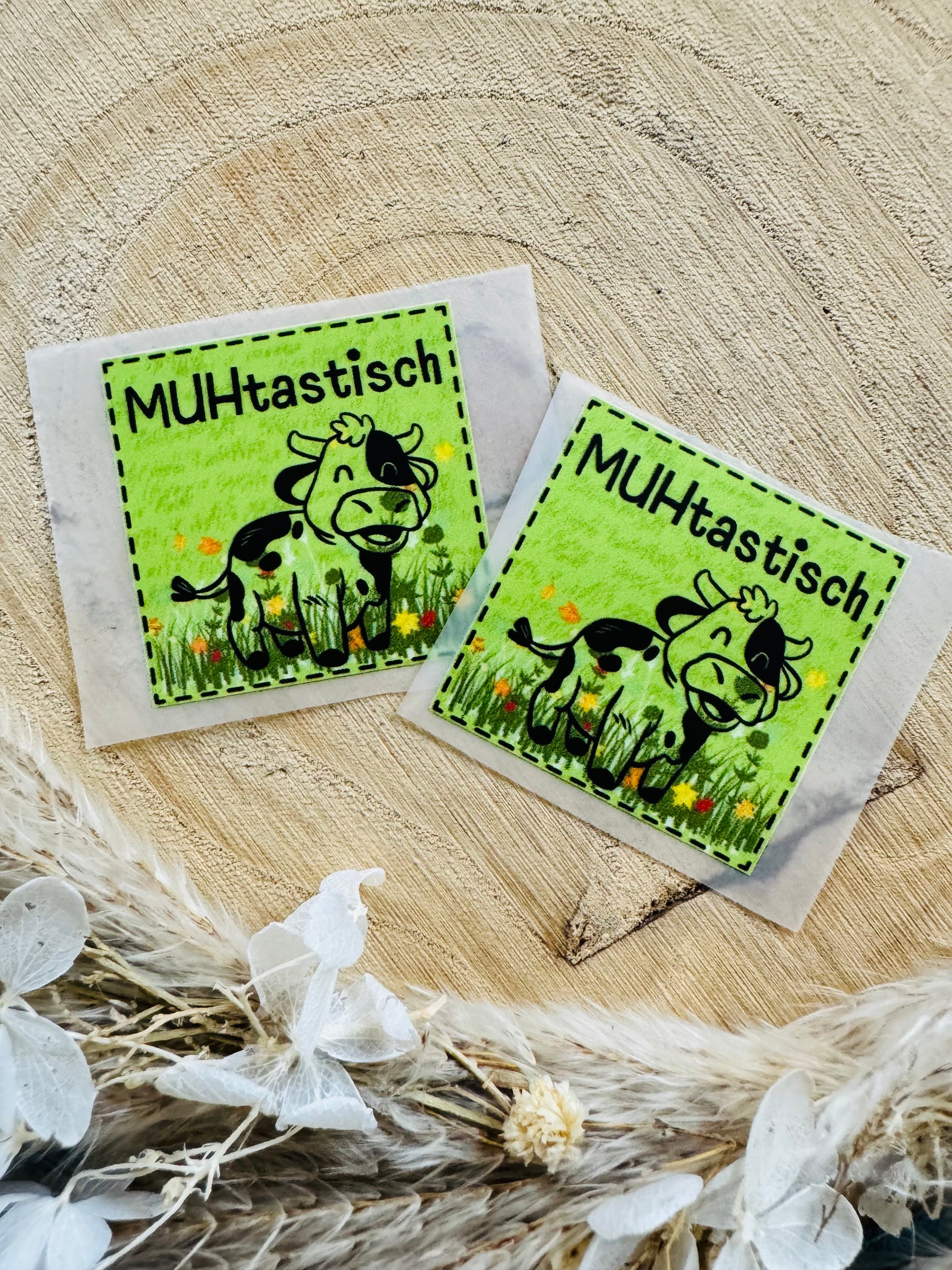 grünes Bügellabel Etikett mit dem Spruch MUHtastisch und einer kleinen Kuh auf einer bunten wiese