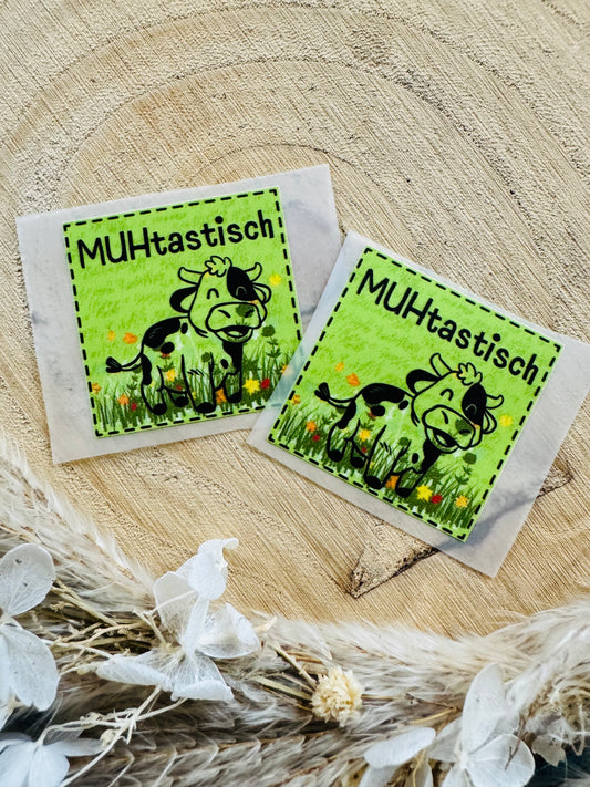 grünes Bügellabel Etikett mit dem Spruch MUHtastisch und einer kleinen Kuh auf einer bunten wiese