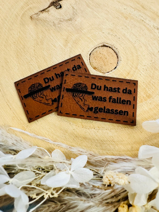superweiches braunes Kunstlederlabel mit dem Spruch Du hast da was fallen gelassen und einer abgebildeten hand mit einem gehirn auf einem Tablett
